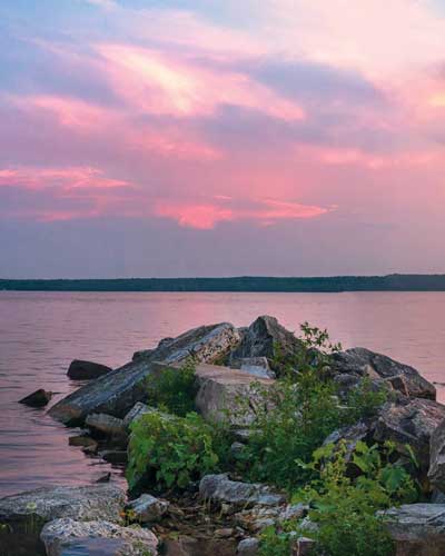 Pink and purple hued sunset over the water with rock formations on the near shoreline taken from Bay Shore Inn of Door County.